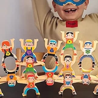 Pyramide d’acrobates en bois colorés emboîtés les uns sur les autres, un enfant souriant au bandeau bleu derrière.