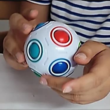 Mains d’enfant tenant une balle blanche à billes de couleur, le casse-tête arc-en-ciel.