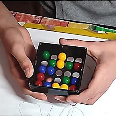 Mains d’enfant tenant une petite boîte noire de billes de couleur alignées sur une grille.