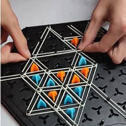 Mains d’enfant tendant des élastiques entre les picots d’un géoplan noir, triangles à pions orange et bleus.