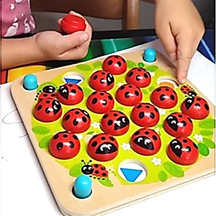 Plateau de jeu en bois aux coccinelles rouges, une main d’enfant en tient une, l’autre en retourne une.