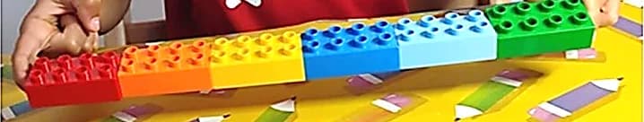La rangée des six briques DUPLO aux couleurs vives, tenue à deux mains au-dessus de la table