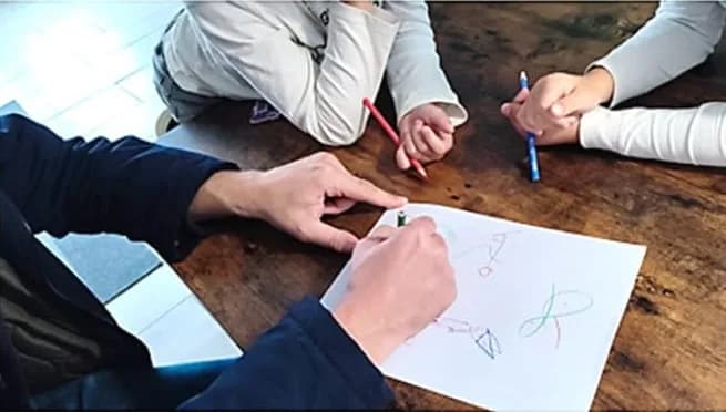 Autour de la table, l'enfant et ses parents partagent un Squiggle de Winnicott au crayon